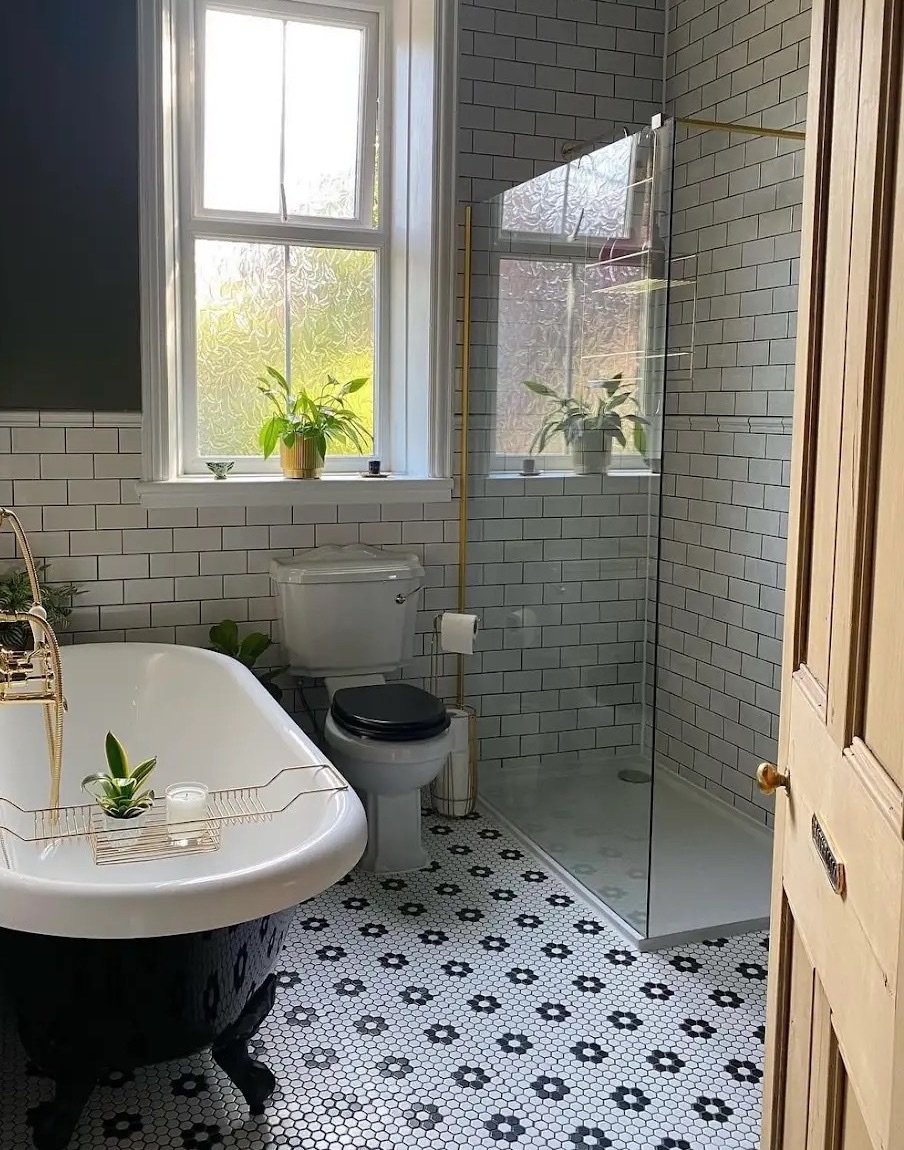 Après : salle de bains en faïence métro blanche, baignoire sur pieds noire à robinetterie laiton, douche ouverte à paroi vitrée et sol en tomettes hexagonales